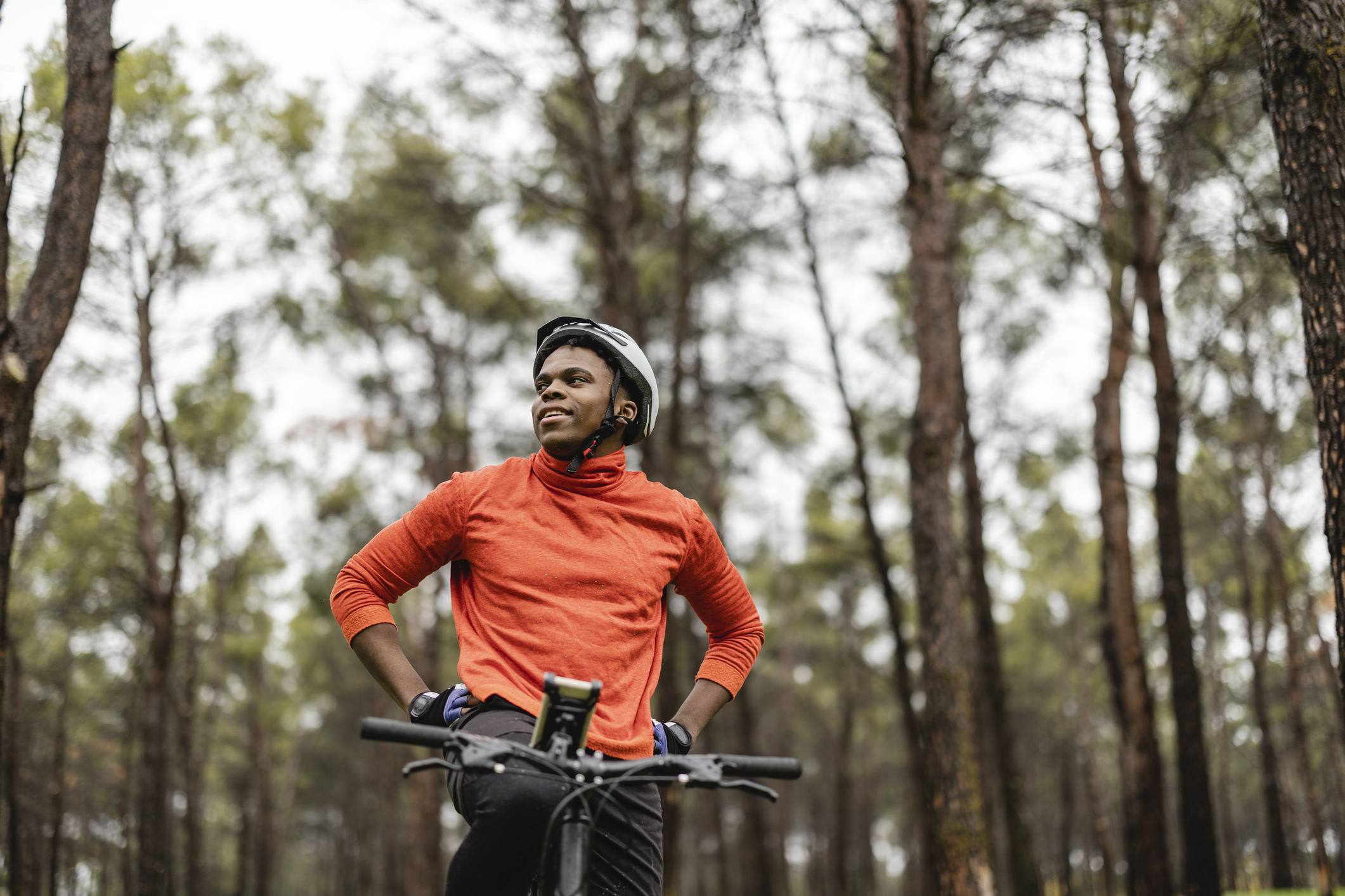 Handsome african american man with a mountain bike standing in the forest, while looking around. He demonstrates a healthy lifestyle.