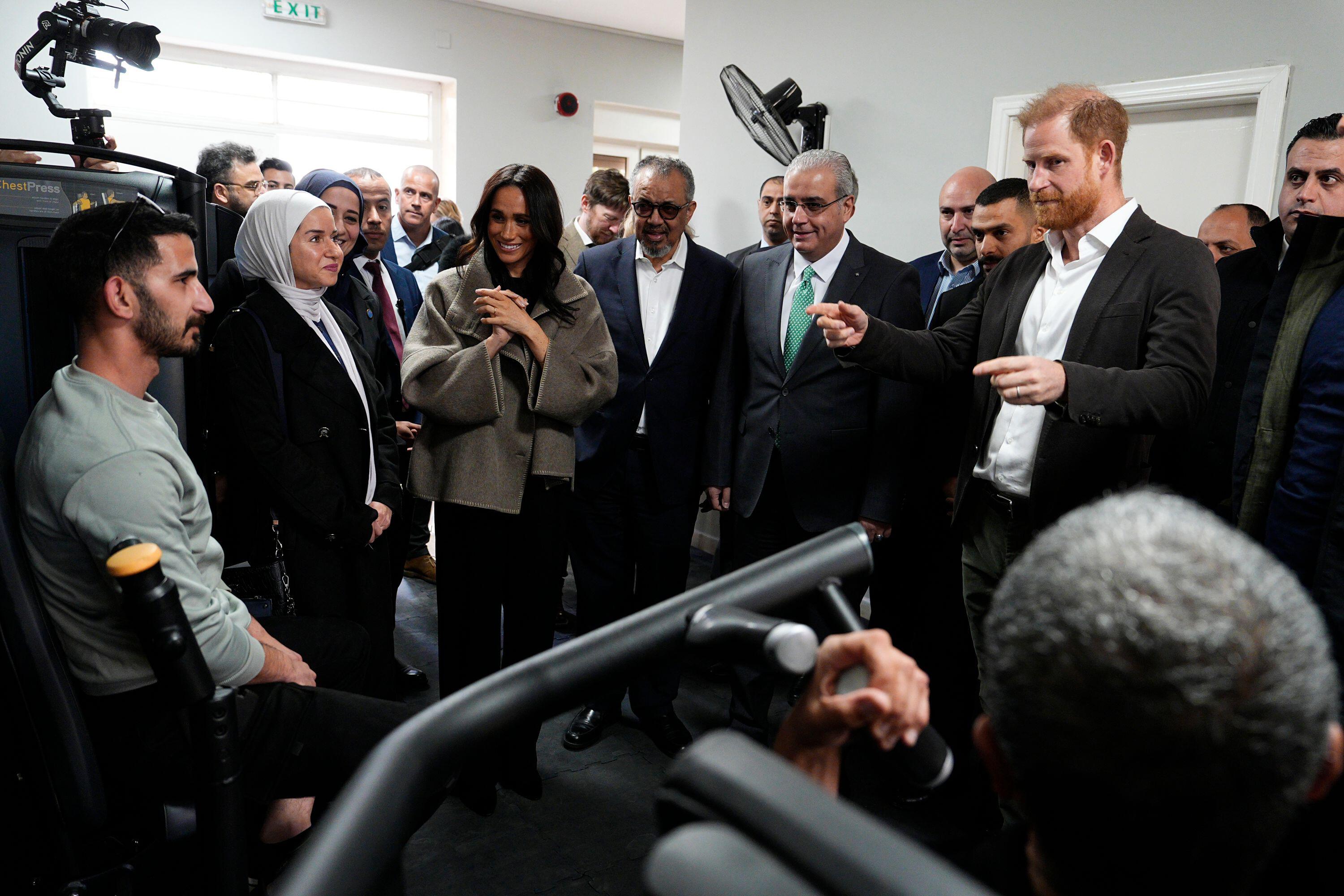 Prince Harry and Meghan Markle standing with a group of people in a gym at an addiction center