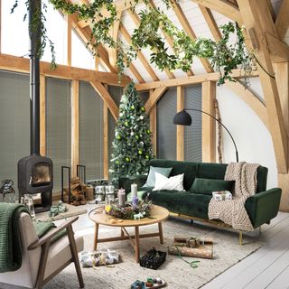 Woodland style Christmas tree in cozy but lofty living room with exposed wood beams, grey couches and a stove