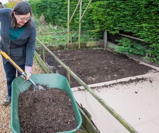 A woman putting compost on top of a no dig vegetable garden bed