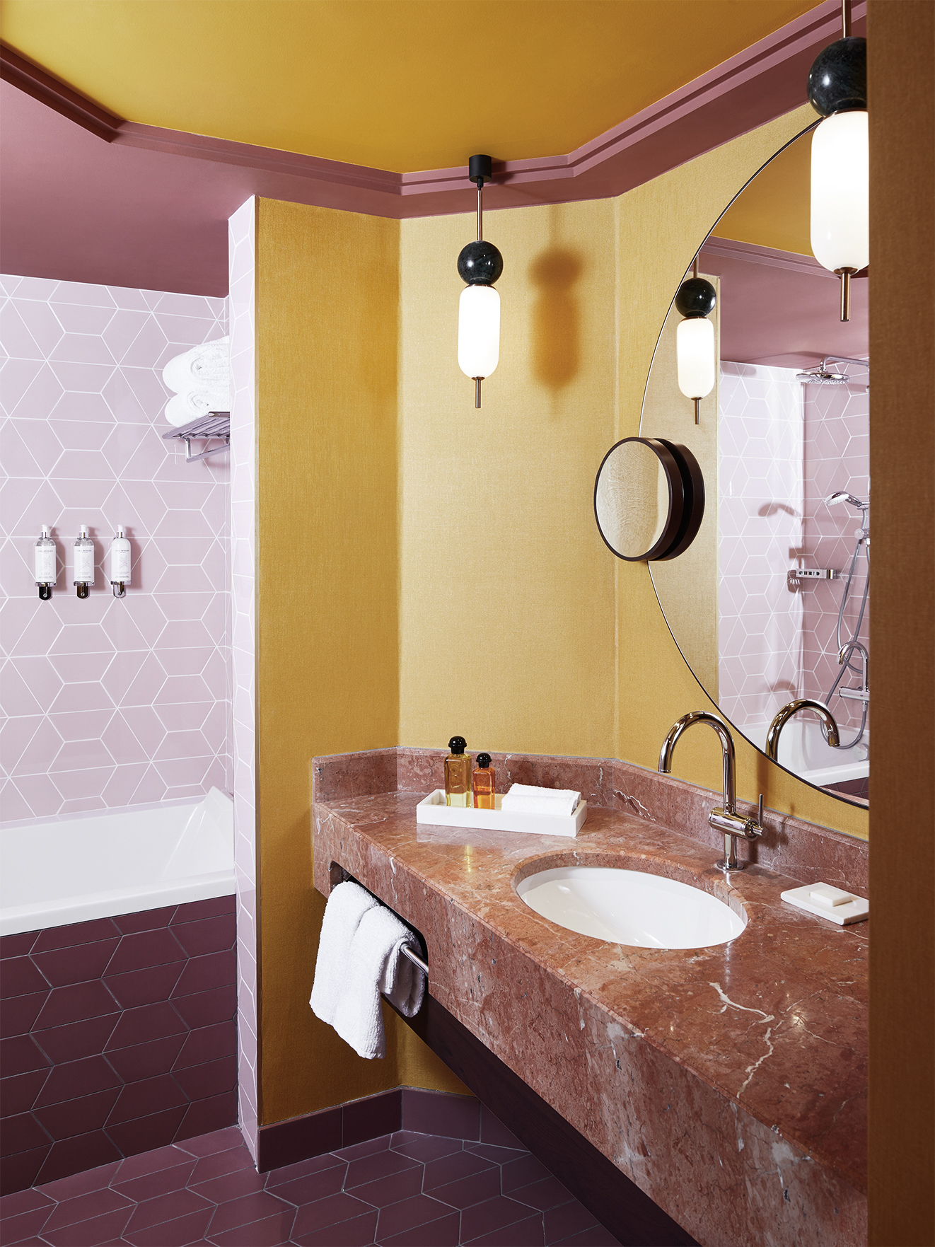 a pink and yellow bathroom with an angular divide and art deco lighting, with a built in bath
