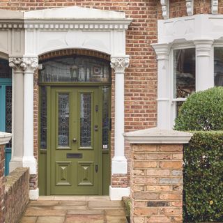 Olive green front door with stained glass panels on a Victorian terrace house.