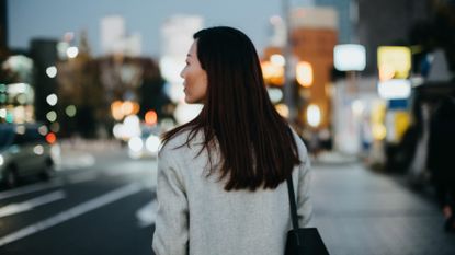 ear view of young woman walking on city street at dusk