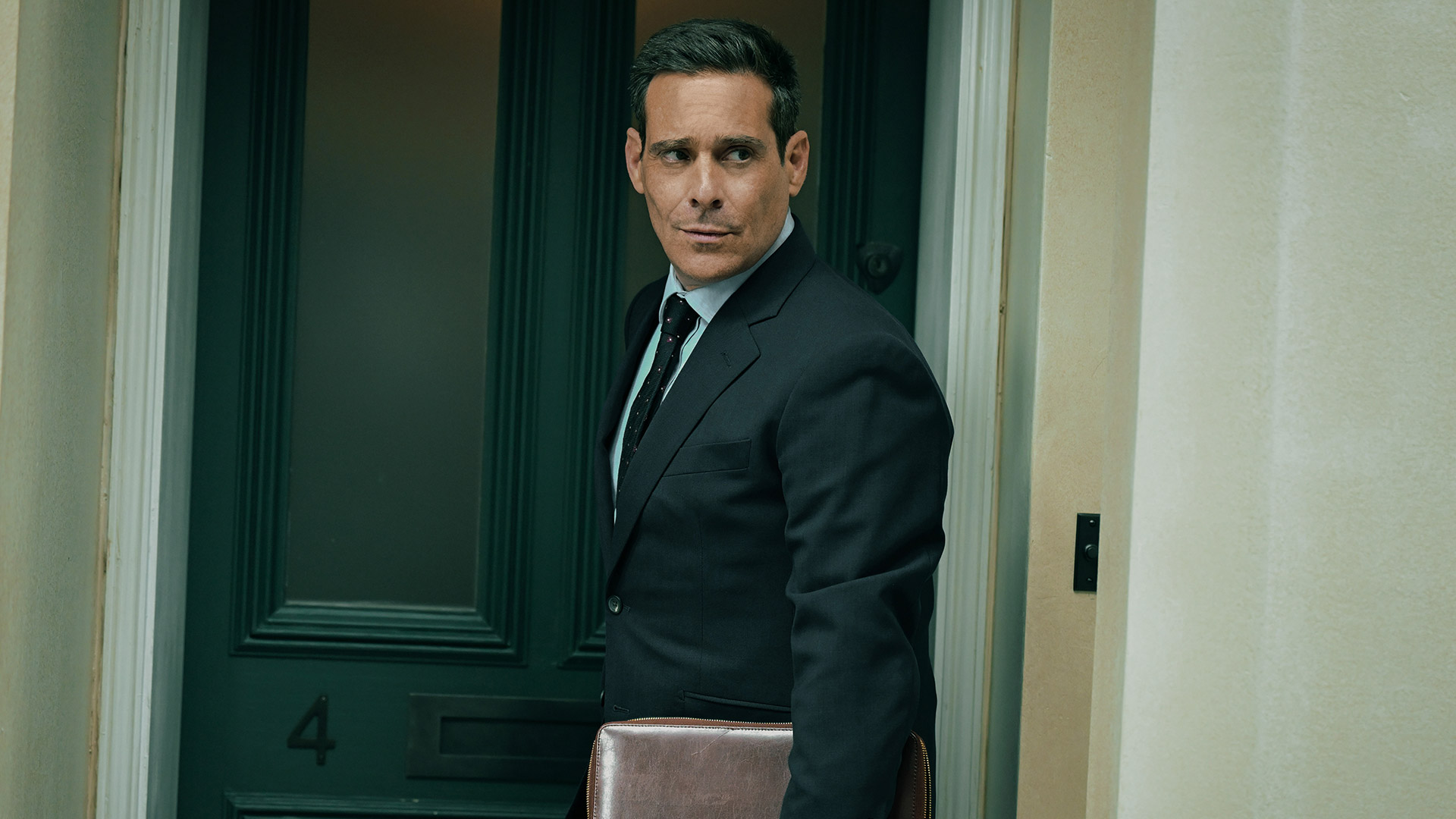 James Callis stands in front of a door while holding a leather bound folder in Slow Horses season 5 episode 4