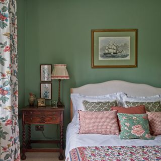 Country style bedroom with green painted walls and mixed patterns on cushions, curtains and bed throw