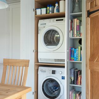 Washing machine and tumble dryer stacked in a cupboard in a white kitchen diner
