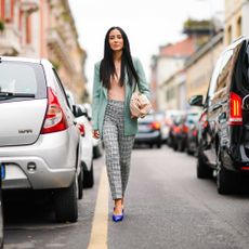 A woman walks in the street wearing a pale green blazer and striped pants