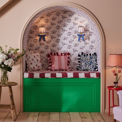 An arched alcove covered in a floral wallpaper with a built-in banquette seating and striped and floral ruffled cushions by Cath Kidston on top