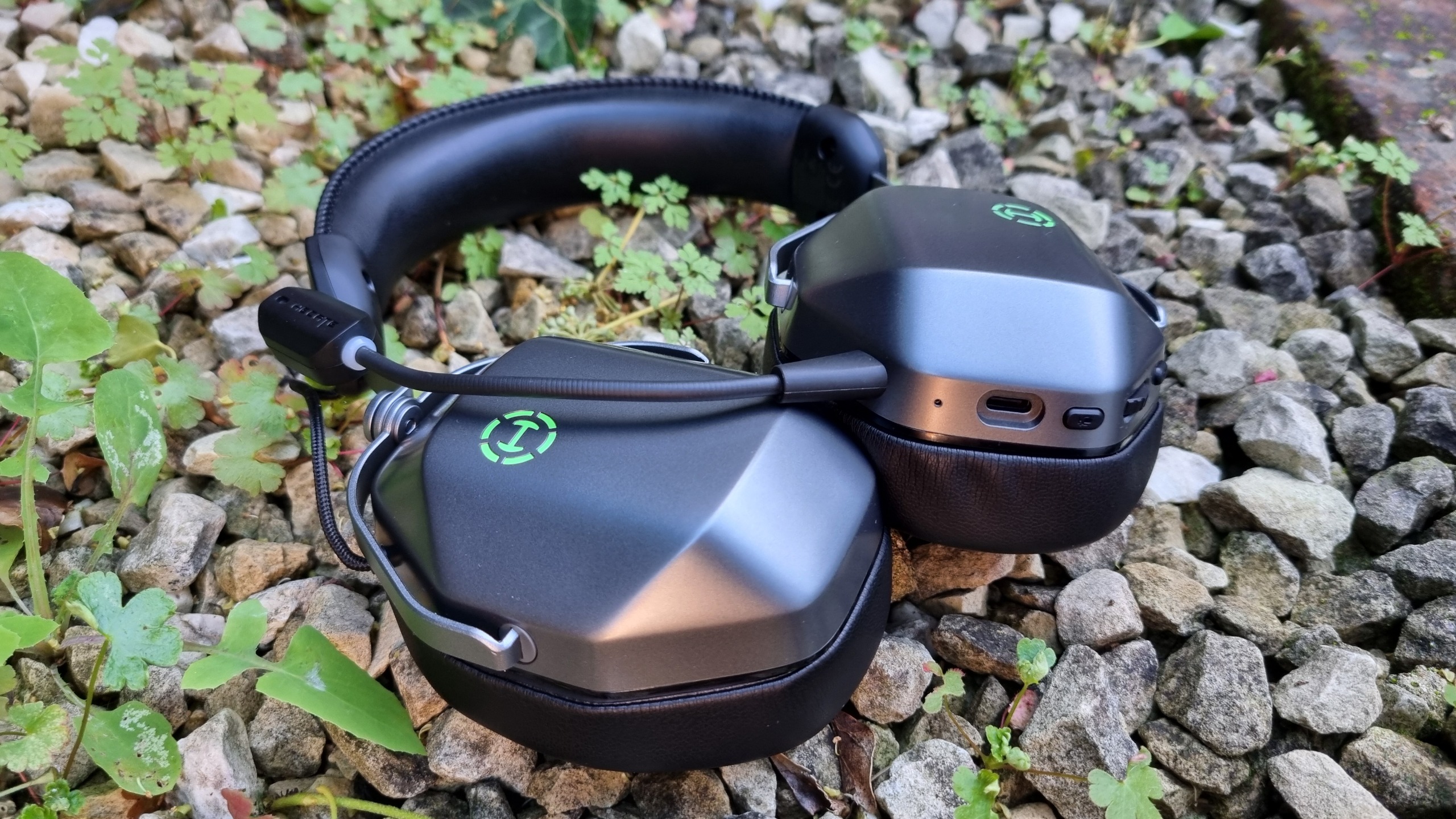 An Edifier G5 Max gaming headset with its RGB lit in green, next to some weeds in a poorly maintained garden