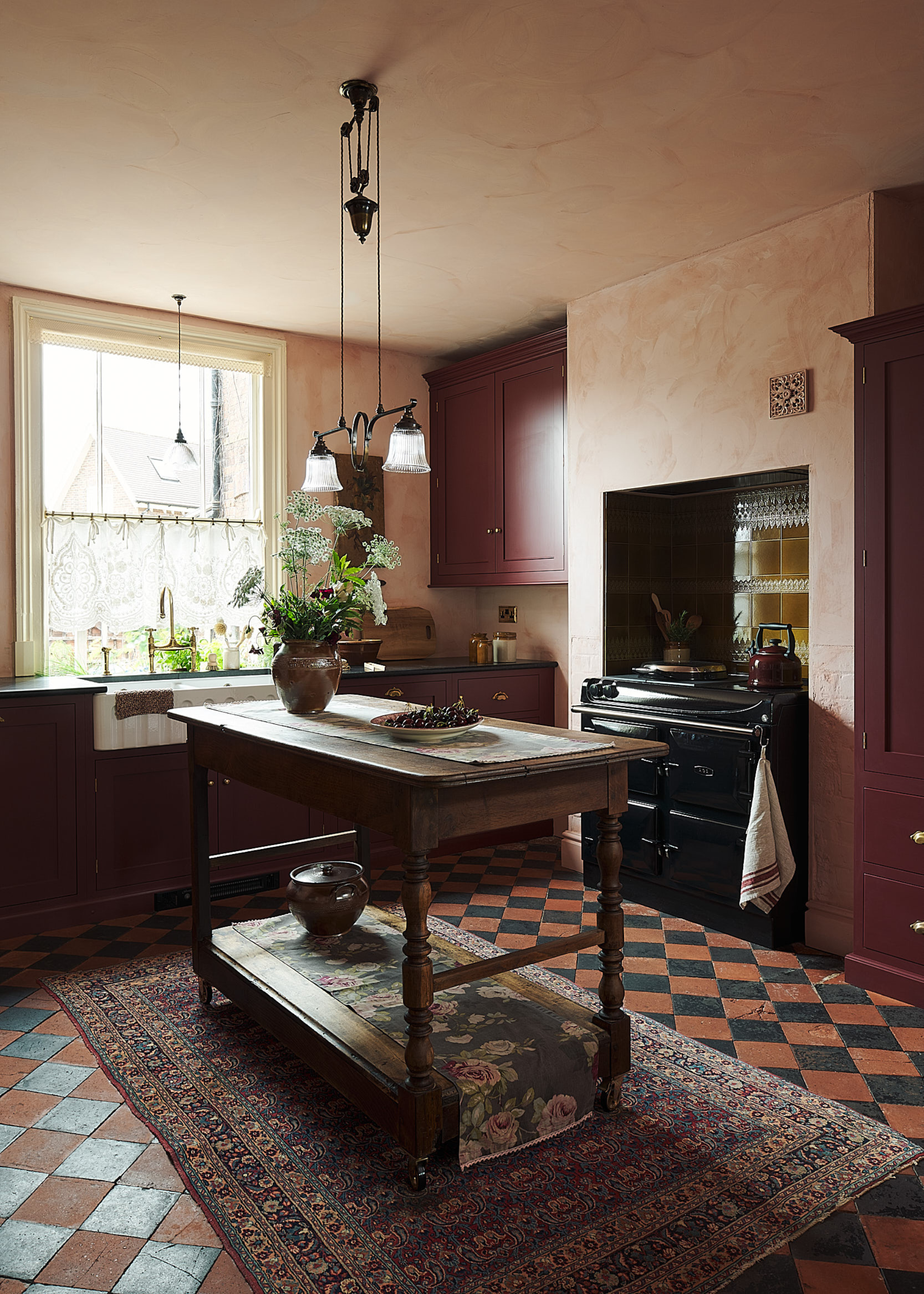 A traditional dark burgundy kitchen with one window, a larger cooker in the alcove and a freestanding antique island
