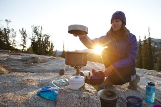 how much fuel to bring backpacking: hiker cooking at sunset