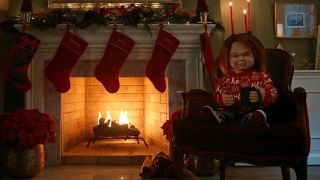 A still of Chucky sat beside a log fire in Chucky Yule Log