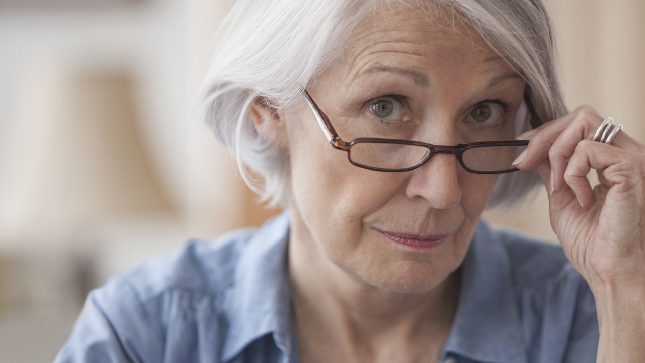 An older woman looks over the tops of her glasses with an interested expression.