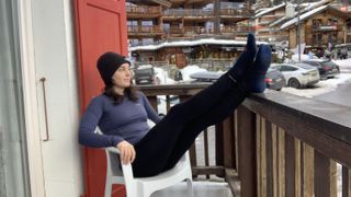 Woman sitting on balcony at ski resort dressed in base layers