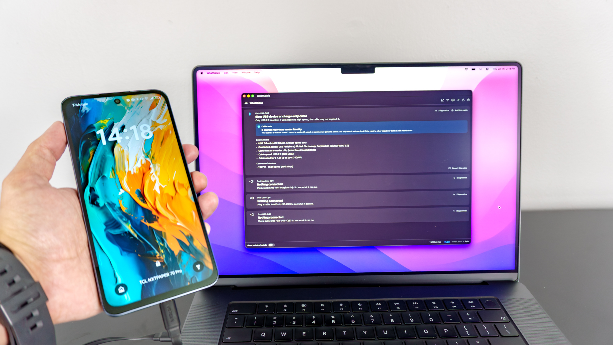 A person holding up a TCL NXTPAPER 70 Pro smartphone connected to a MacBook Pro running the WhatCable app