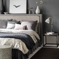 A grey painted bedroom with a dark grey rug next to a grey bed with grey bed linen