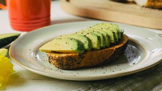 A slice of toast on a plate with sliced avocado on top of it