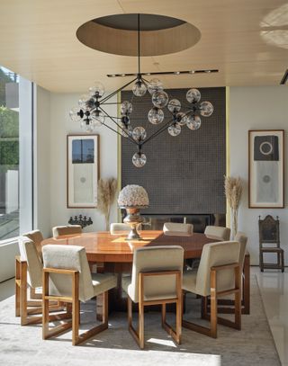 A dining room with a circular table, a floral centerpiece and statement lighting