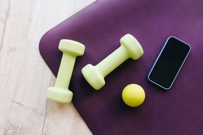 a couple of dumbbells, a yellow ball, and phone on an exercise mat