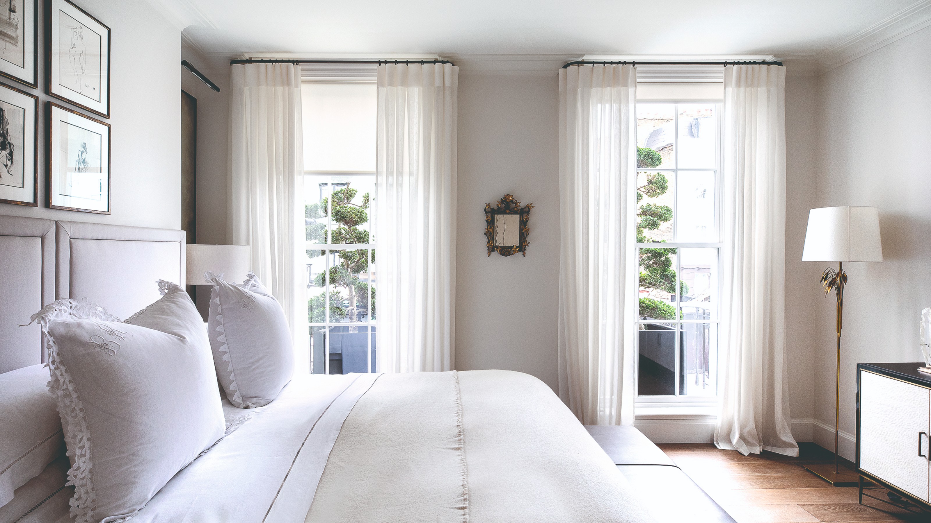 A white bedroom with voile curtains on the windows and white bed linen