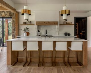 Kitchen with wood island and bar chairs, veined countertops, range with backsplash, white walls and wood floor