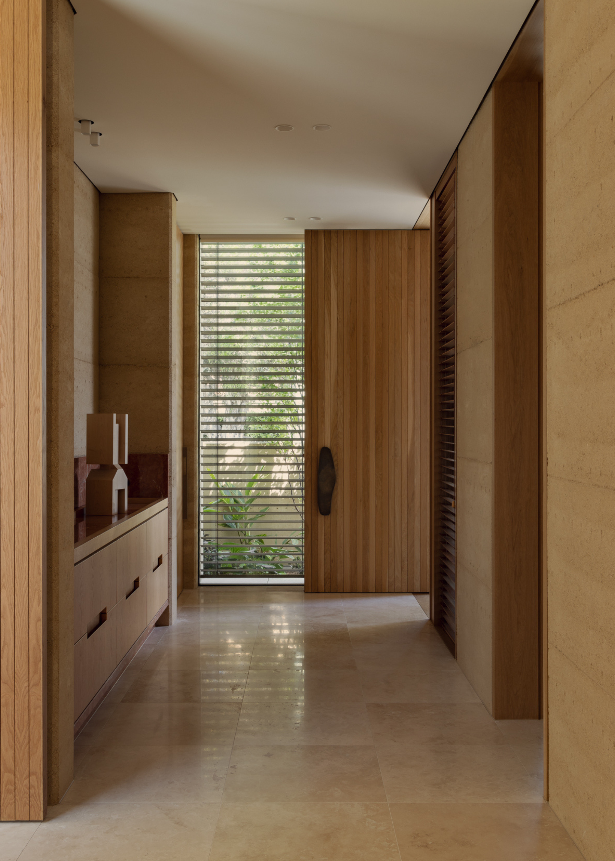 A minimalist entryway with slatted windows, a bold wood handle, and structured wood decor