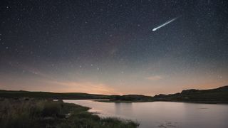 A single bright meteor streaks over a pond at night