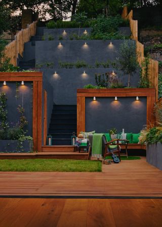 Sloped backyard ideas in a wooden design with black slate terraces and steps and downlighters.