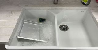 ceramic double sink with one side filled with hot soapy water and sponge to show how to clean oven trays with ease