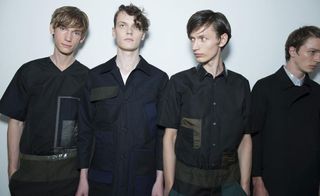 4 male models wearing dark coloured clothing standing in a studio