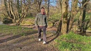 Man strolling along a riverbank wearing Merrell SpeedArc Surge Boa walking shoes