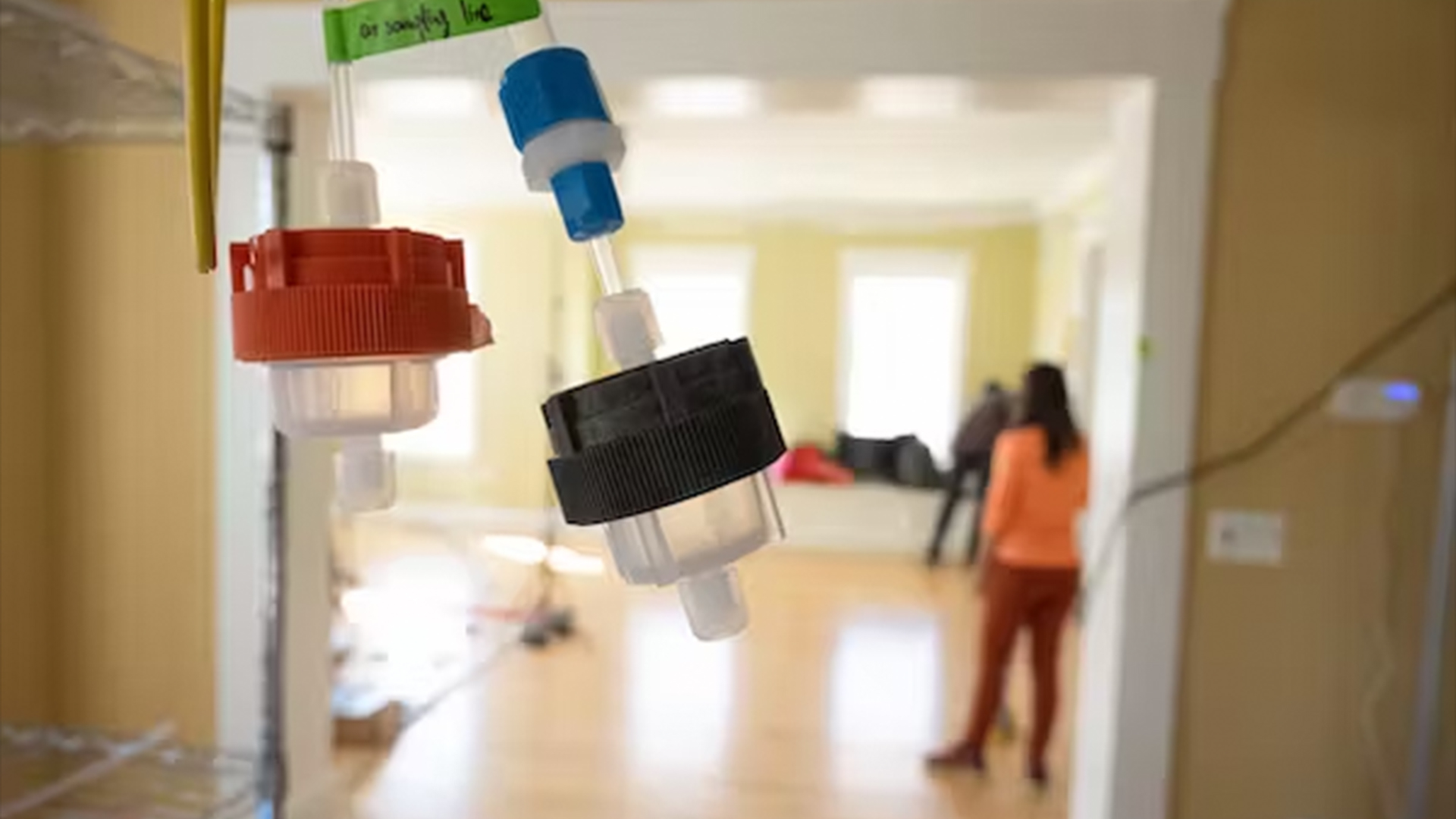 small plastic containers shown strung up throughout a house, with researchers in the background