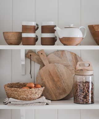 A close up of white open shelving with a variety of kitchen items such as cutting boards and storage jars on them