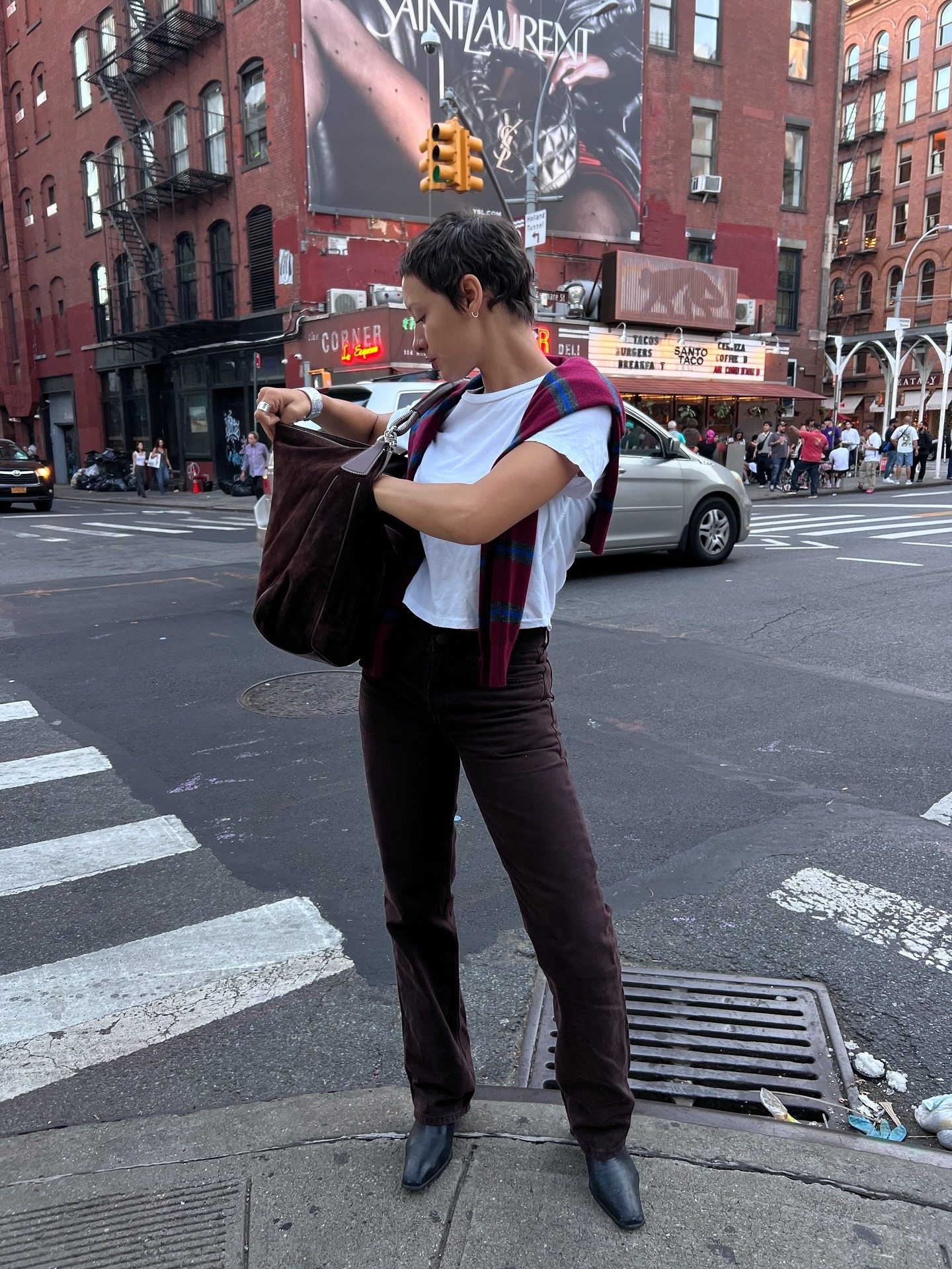 Fashion person Aisha Farida wears best squared toe boots. She pairs her boots with corduroy brown jeans, a white tee and red and blue striped jumper. In an image in New York, she is stood looking into her bag in front of a big billboard and red brick buildings. This image was recently taken from her Instagram.