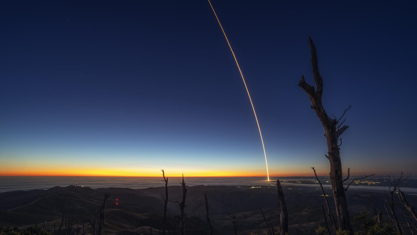 a rocket launches at night, leaving a streak of light through the sky