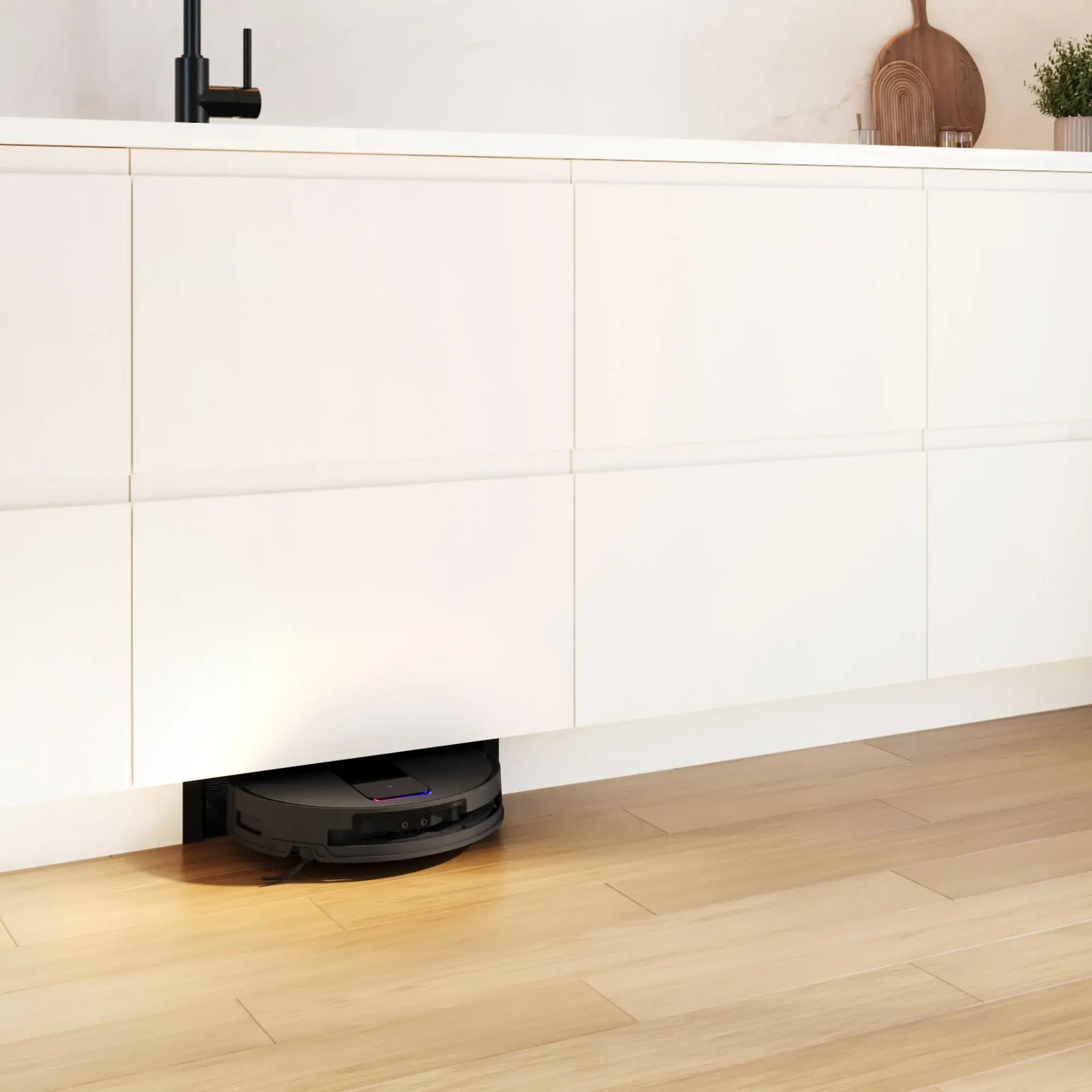 Bosch integrated robot vacuum and mop in a white kitchen with white cabinets and light wood flooring