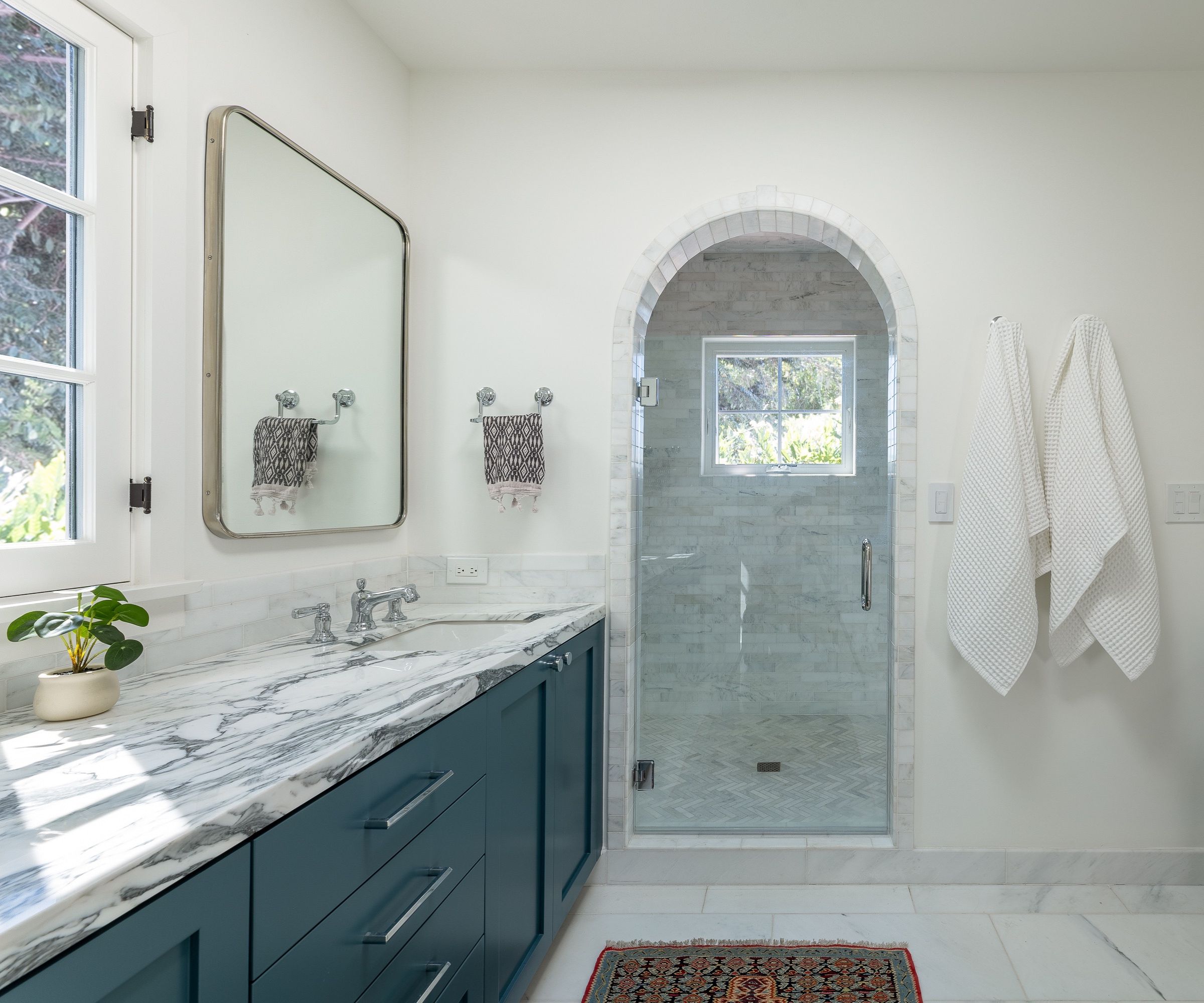 A large bathroom with white walls, dark blue vanity units and marble countertops