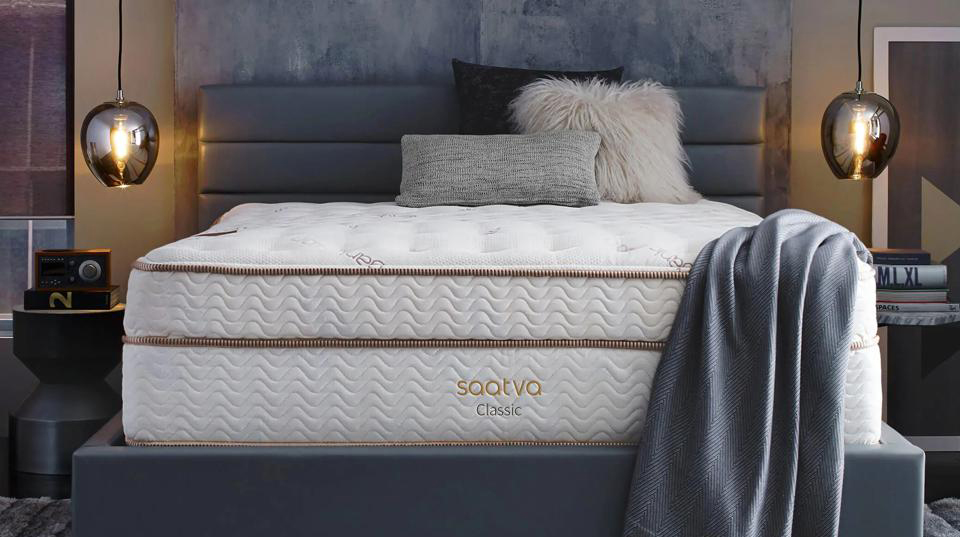 The Saatva Classic mattress with a gray blanket draped over one side