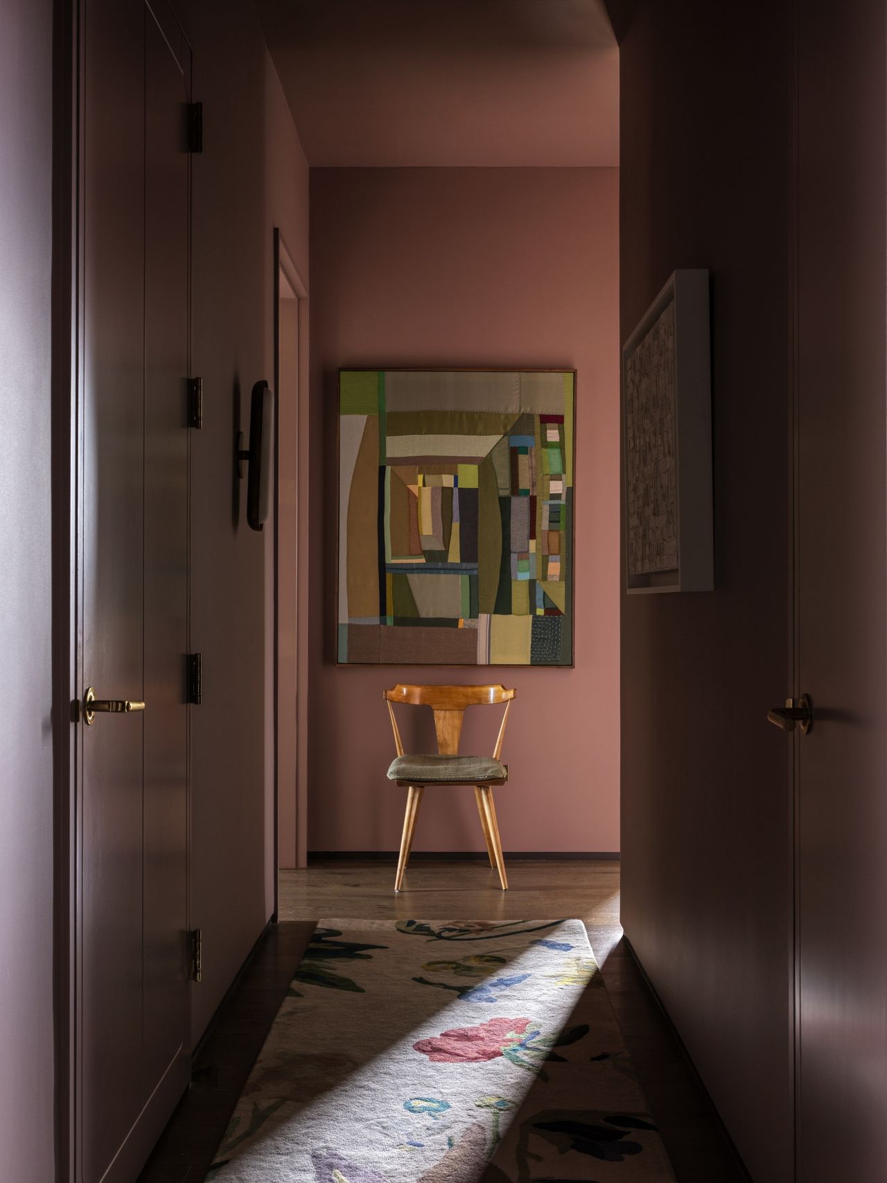 hallway with pink walls, colorful artwork, stool, and patterned runner