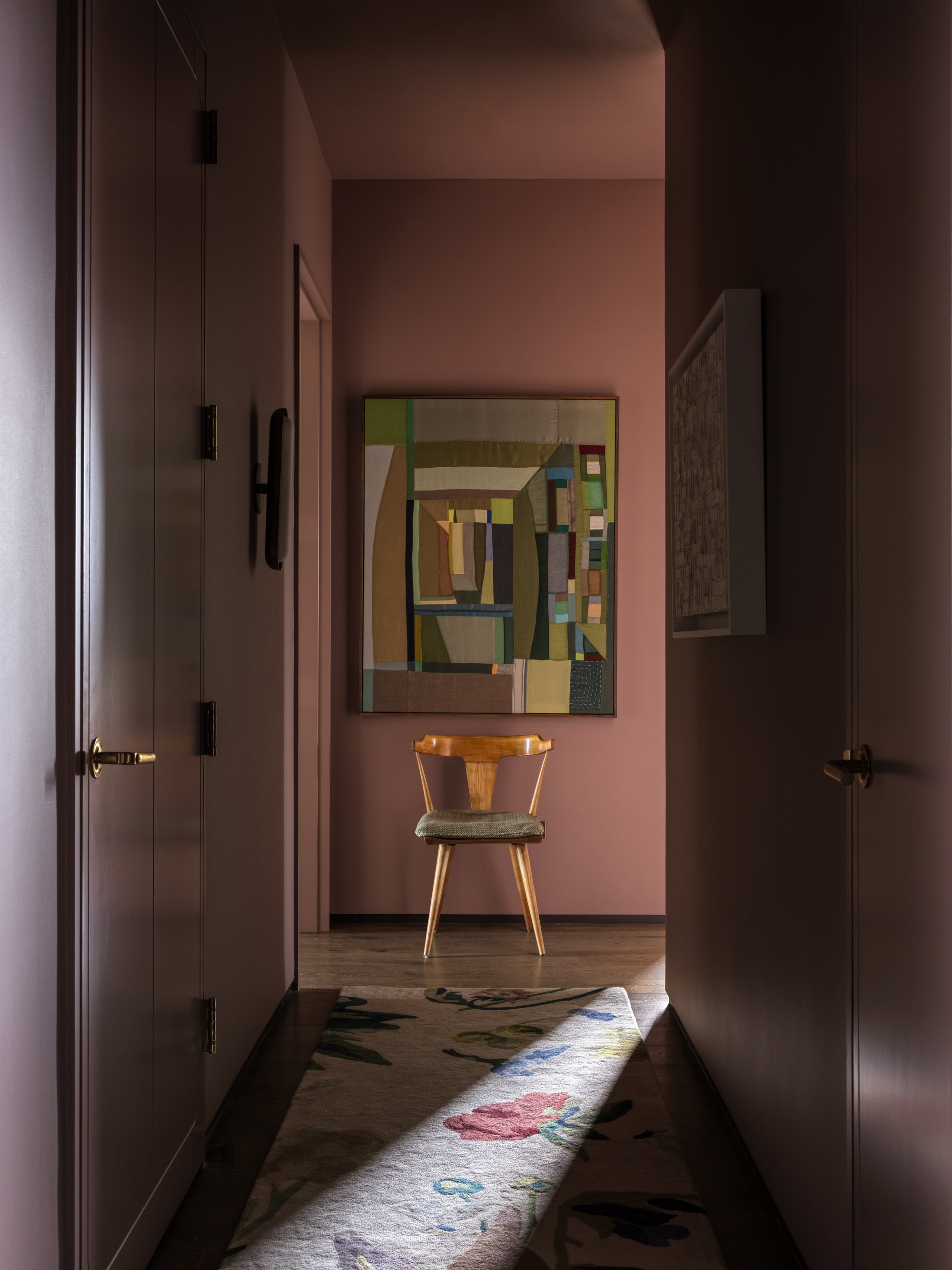 hallway with pink walls, colorful artwork, stool, and patterned runner