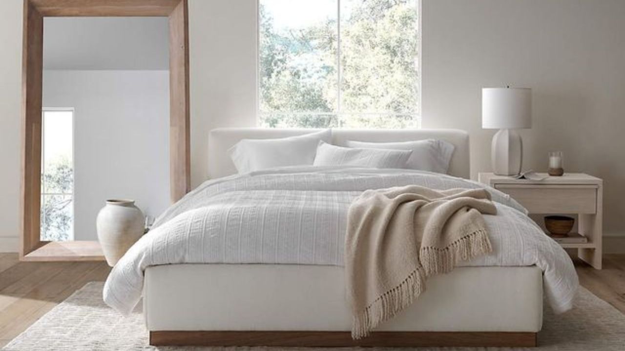 The cloud bed recipe, as seen on a Crate &amp; Barrel bed: an oversized comforter, plush pillows and a fluffy throw on a bed against a white wall and a big bedroom mirror.