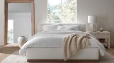 The cloud bed recipe, as seen on a Crate & Barrel bed: an oversized comforter, plush pillows and a fluffy throw on a bed against a white wall and a big bedroom mirror.