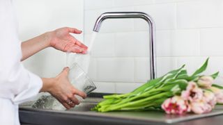 picture of woman filling a vase with water to put tulips in to support the denture tablet hack for flowers