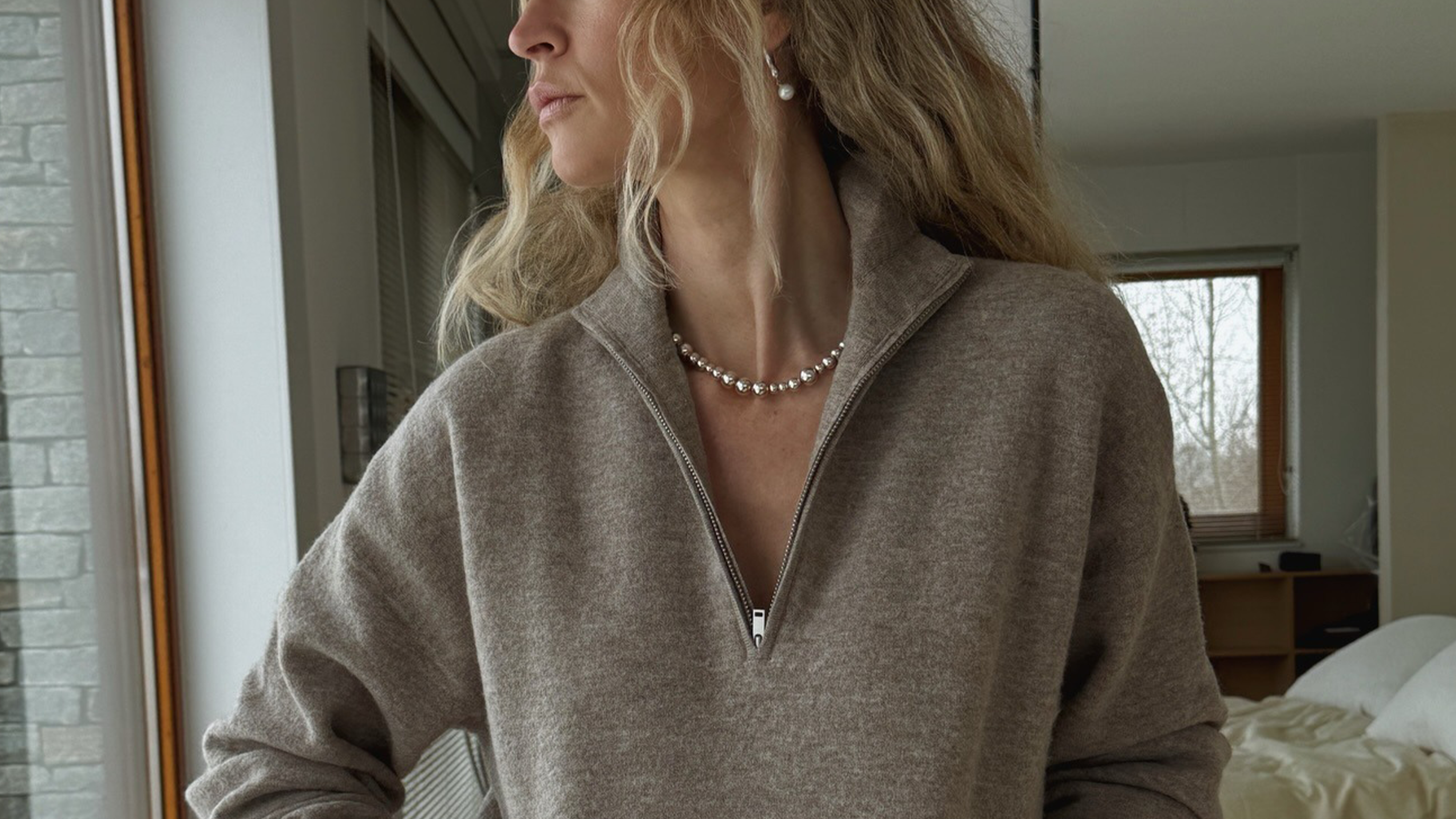 Woman wearing brown quarter-zip sweater outfit with jeans, sweater, and pearl necklace.