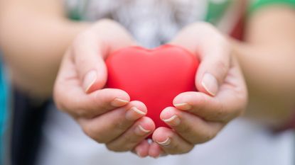 A person holds out a red heart. 