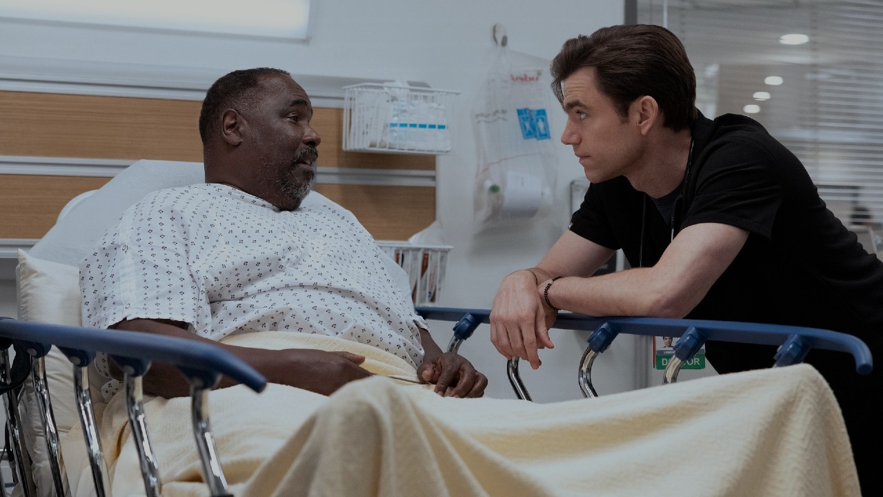 病院のベッドに座るルイと、その右側に寄りかかるラングドン。