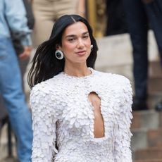 a paparazzi photo of a woman with long, black hair wearing a frilly white pantsuit