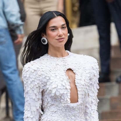 a paparazzi photo of a woman with long, black hair wearing a frilly white pantsuit