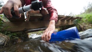 Person filling up a water bottle from a stream