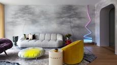 Living room with grey nature scene mural, grey sofa, yellow armchair, neon zig-zag wall light and neon and grey footrest